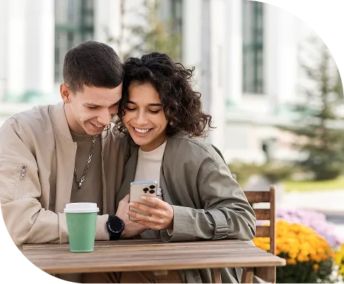 Couple at a table outdoors looking at a phone together and smiling