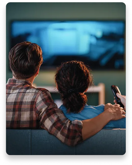 Back of couple on couch watching movie. Man has arm around woman.